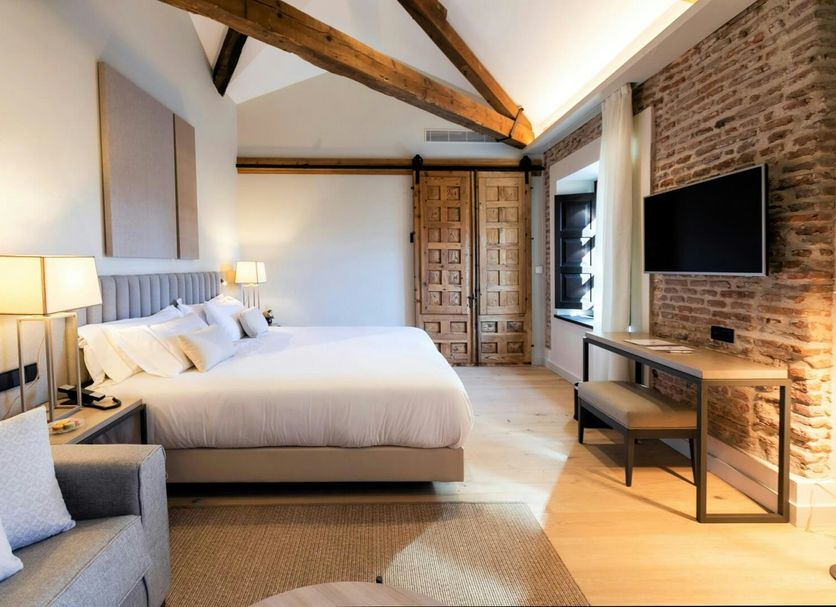 Sofraga Palacio in Ávila guest room with king bed, exposed beams, brick wall, and wall-mounted TV