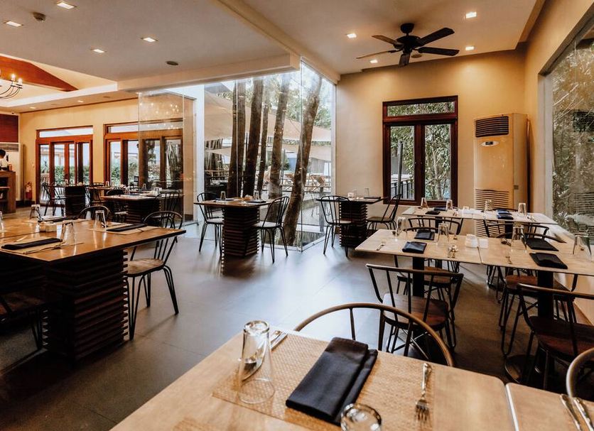 The Funny Lion Coron dining area with tables, large windows, and a view of trees outside