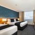 Hotel Diana Woolloongabba room in Brisbane with two beds, armchair, desk and city view through curtains