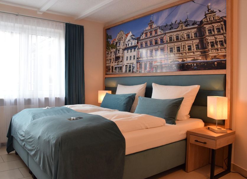 Hotel Garni Am Domplatz in Erfurt bedroom with double bed, teal bedding, bedside lamps and city artwork