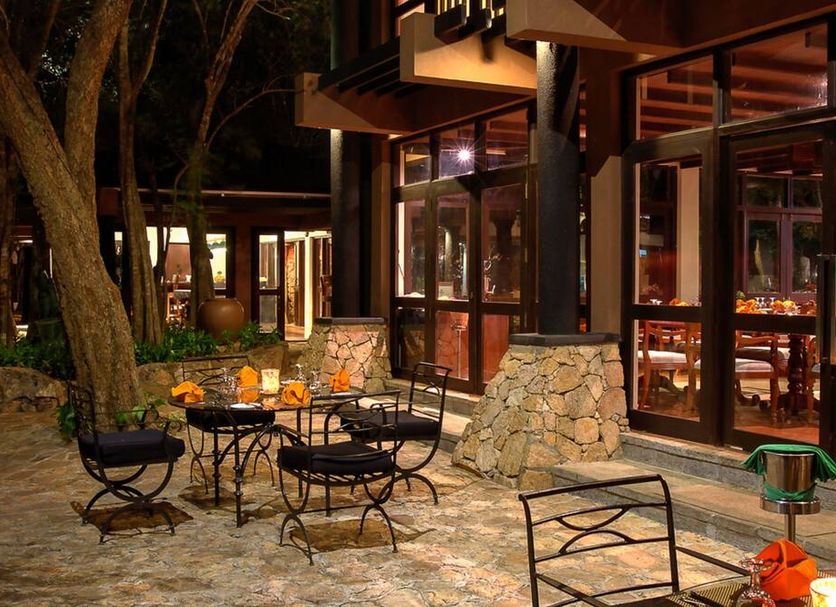 The Deer Park Hotel in Giritale: outdoor patio with tables, chairs and warm-lit glass-fronted building