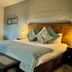 River Crossing Lodge Windhoek bedroom with king bed, bench, armchairs and mountain-view window