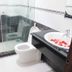Ban Mai Hotel 66, Phan Thiet bathroom with glass shower, toilet, and sink with flower petals