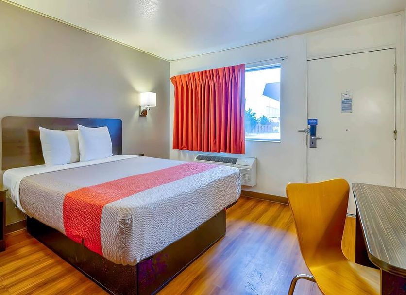 Motel 6 Santa Rosa Nm guest room with king bed, red curtain, and wood-look floor in Santa Rosa