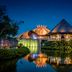 Jungala Hotel at VidantaWorld Riviera Maya in Cancún with illuminated thatched buildings reflected on the water
