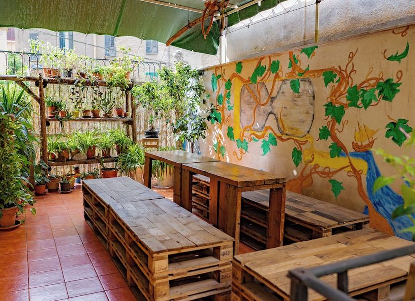 A Casa di Amici Palermo courtyard with mural wall, plants, and rustic wooden tables