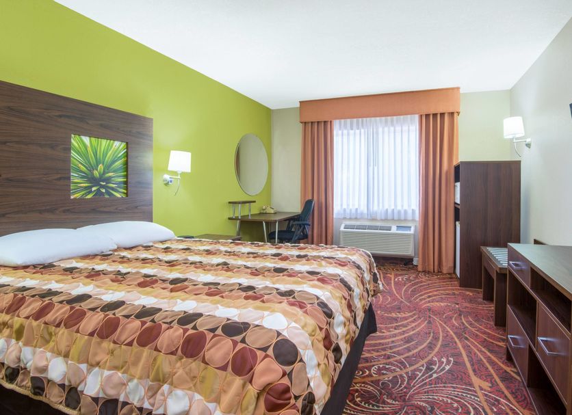 Super 8 by Wyndham Portales guest room with king bed, TV, desk, window air conditioner and patterned carpet