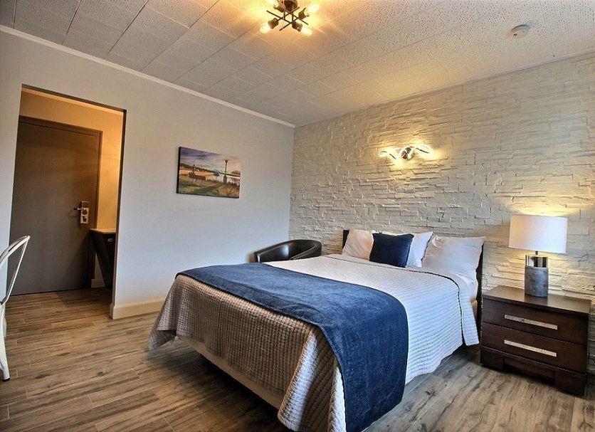 Hotel Motel Le Quiet in Lac-Mégantic: guest room with queen bed, bedside lamp, wall art and wood flooring
