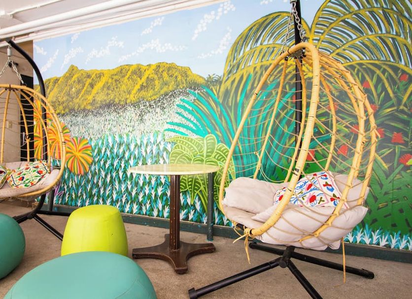 Waikiki Beachside Hostel in Honolulu lounge with hanging chairs and tropical mural