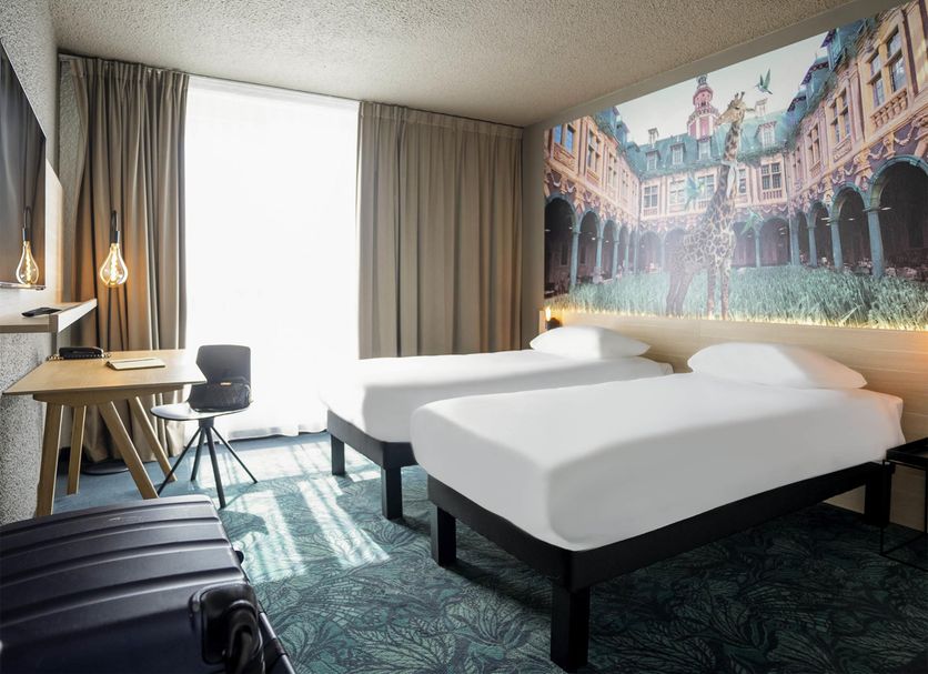 ibis Styles Lille Neuville en Ferrain room with two beds, desk, and cityscape mural in Neuville-en-Ferrain