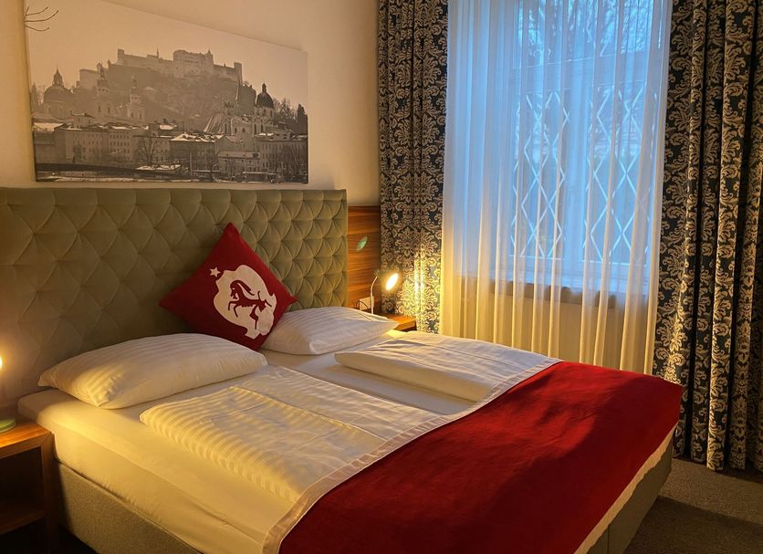 Hotel Villa Carlton Salzburg room with tufted bed, red accents, and castle wall art by a window