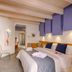 Hospitality Hotel Palermo guest room with king bed, purple wall panels, and wood-beam ceiling