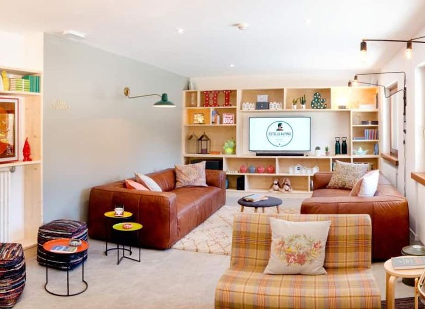Ostello Alpino Bormio lounge with leather sofas, shelving, TV and plaid armchairs