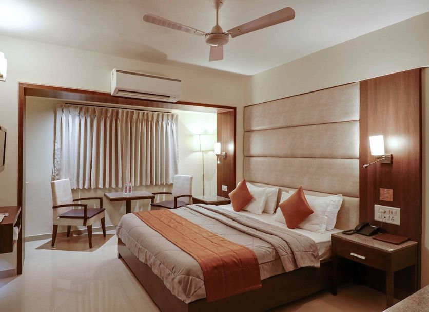 Hotel Centra-Ahmedabad room with a king bed, ceiling fan, seating area, and wall-mounted TV in Ahmedabad