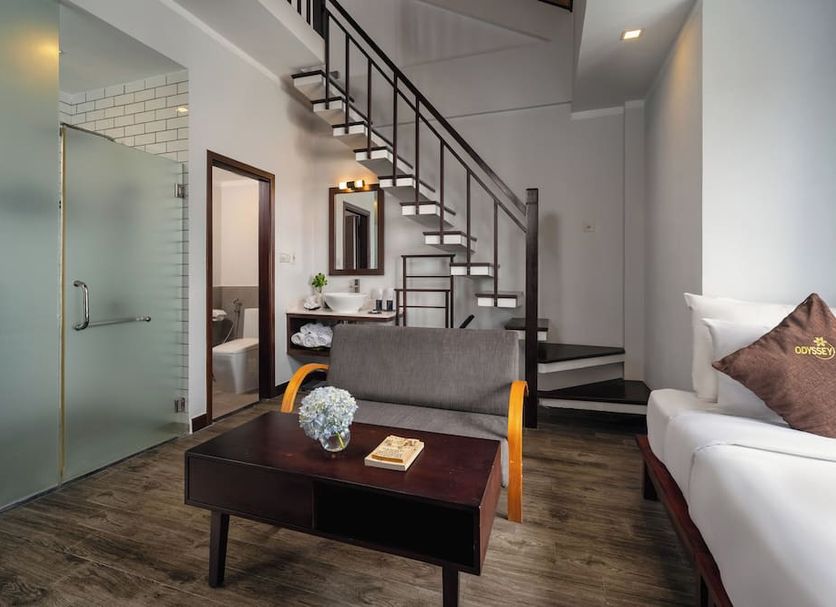 Hoi An Odyssey Hotel in Hoi An room with loft stairs, seating area, glass bathroom, and bed