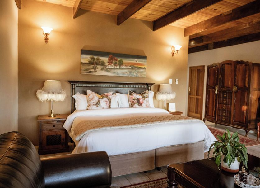 De Denne Country Guest House in Oudtshoorn bedroom with king bed, wood-beamed ceiling and armoires
