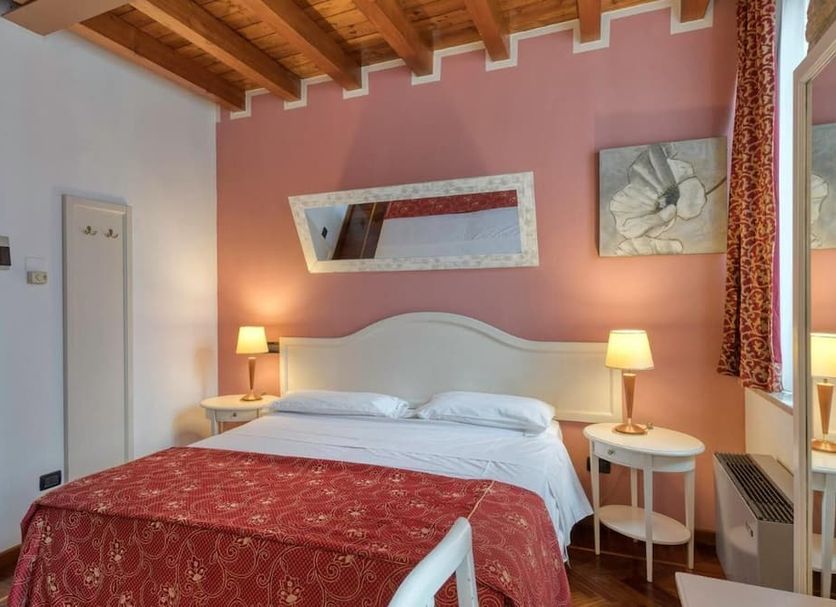 Primotel Brescia guest room with double bed, bedside lamps, pink accent wall and wood beam ceiling in Brescia