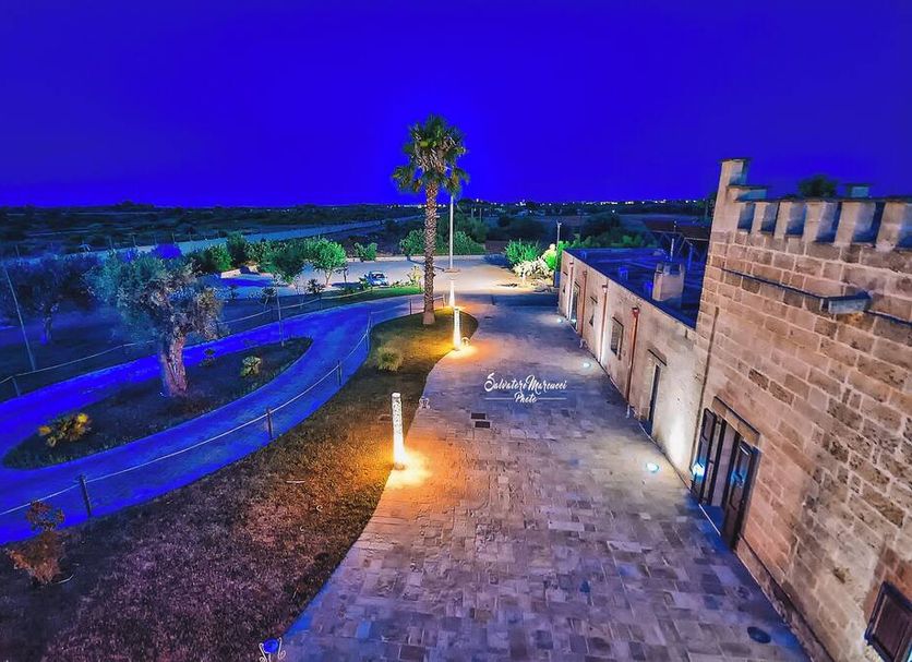 Masseria Tenuta Quintino in Porto Cesareo with a lit stone terrace and palm-lined pool area at dusk