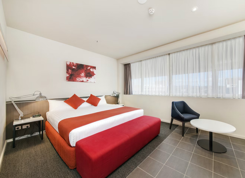 Abode Woden Canberra room with king bed, red bench, chair and large windows with city view