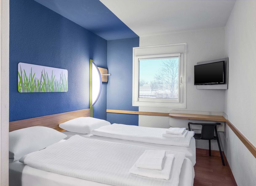 B&b Hotel Erlangen-tennenlohe room with twin beds, blue accent wall, window and wall-mounted TV in Erlangen