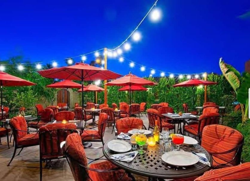 Los Arboles Hotel in Palm Springs outdoor patio dining with red umbrellas and string lights at dusk