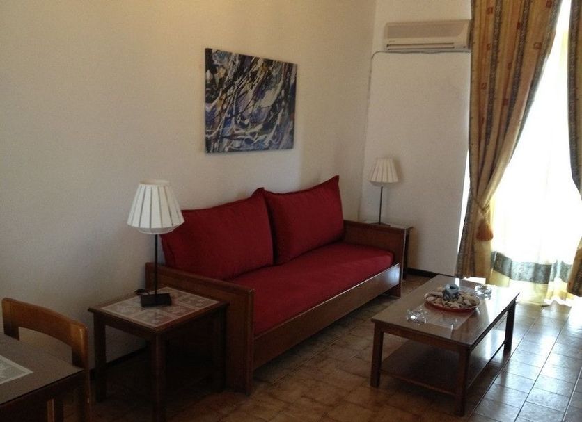 Gythion Hotel in Gytheio: red sofa, coffee table and lamp in a simple sitting area by a window.