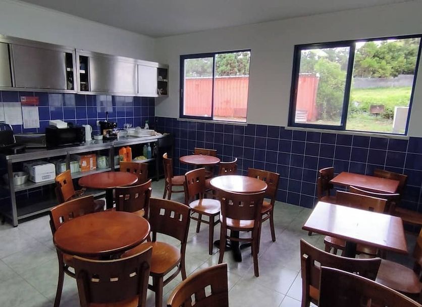 Hospedaria Jsf in Horta: communal dining area with tables, chairs, kitchenette, and large windows