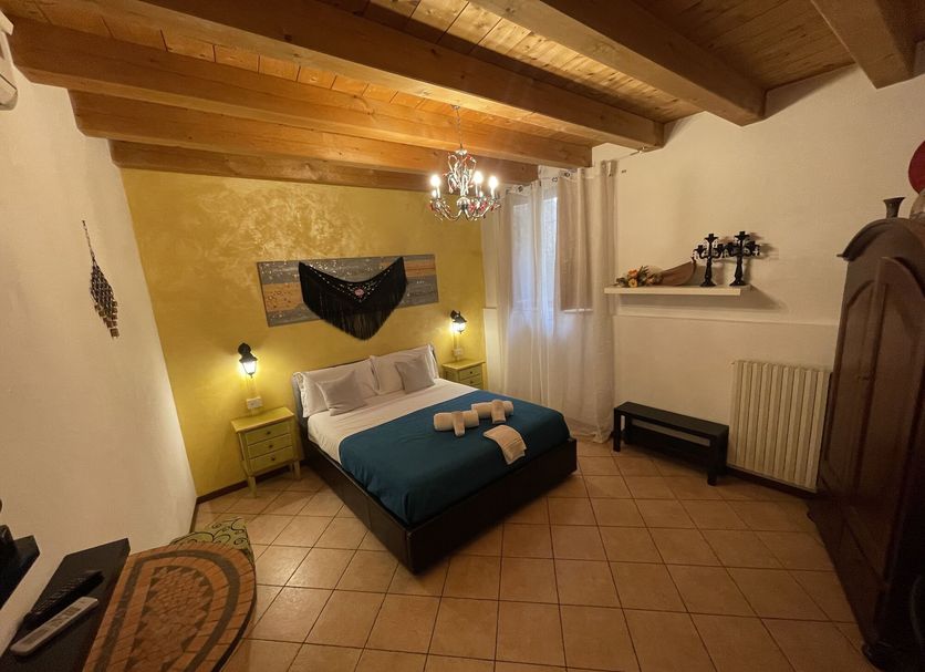 Vicolo 22 in Verona guest room with exposed wood beams, bed, tiled floor and chandelier