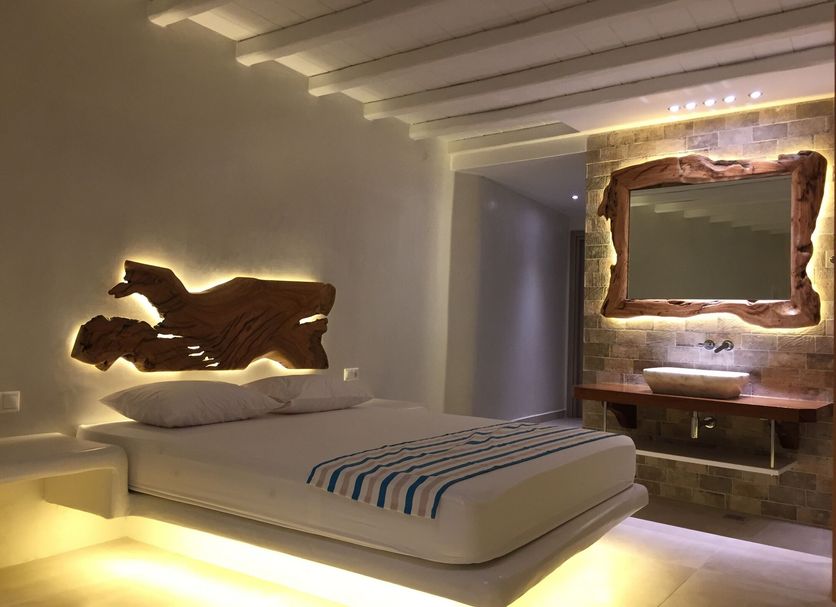 Eternal Suites in Mykonos bedroom with carved wood wall art, lit mirror vanity and low bed