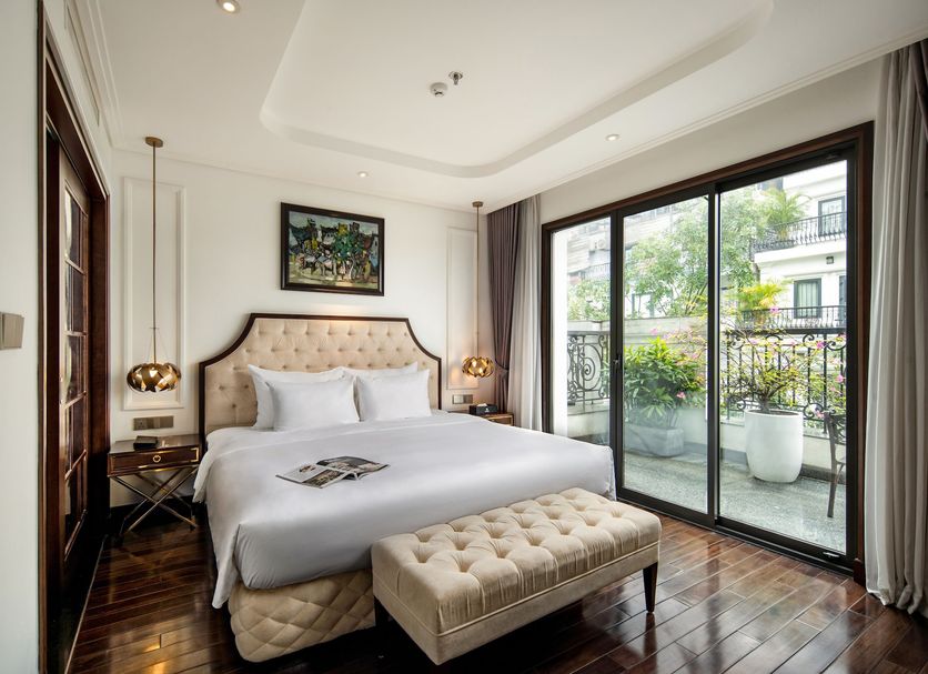 Anatole Hotel Hanoi guest room with tufted bed, bench, and balcony overlooking Hanoi greenery
