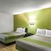 Motel 6 Augusta KS guest room with two beds, lime-green accent wall and wood-look floor in Augusta