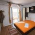 Apartments Alissa in Hvar, bedroom with orange bedspread, balcony door, and wardrobe storage