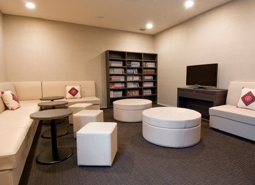 Dormy Inn Nagasaki Shinchichukagai lounge with sofas, round ottomans, shelves and TV in Nagasaki