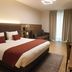 Threeland Hotel Pétange guest room with king bed, sofa, desk, and floor-to-ceiling curtains