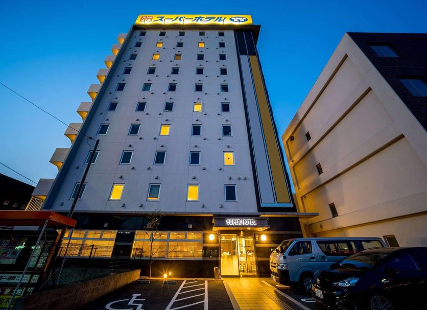 Super Hotel Hofu-Ekimae in Hōfu, exterior view of tall hotel building at dusk with entrance and parking