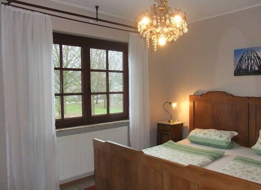 Landhaus Nalbach guest room with wooden bed, chandelier, and window view of greenery