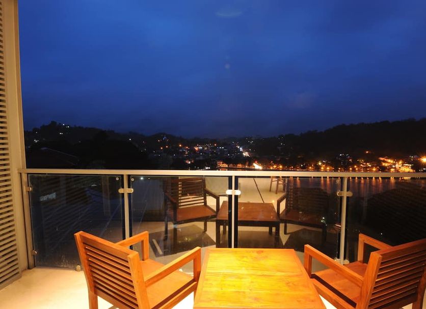 Oak Ray Heritage Hotel in Kandy balcony with wooden chairs and table overlooking city lights at dusk