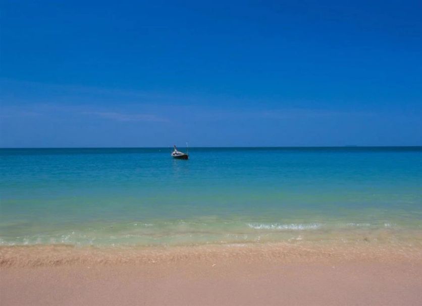 Relax Beach House in Ko Lanta with calm turquoise sea, sandy beach, and a small boat offshore