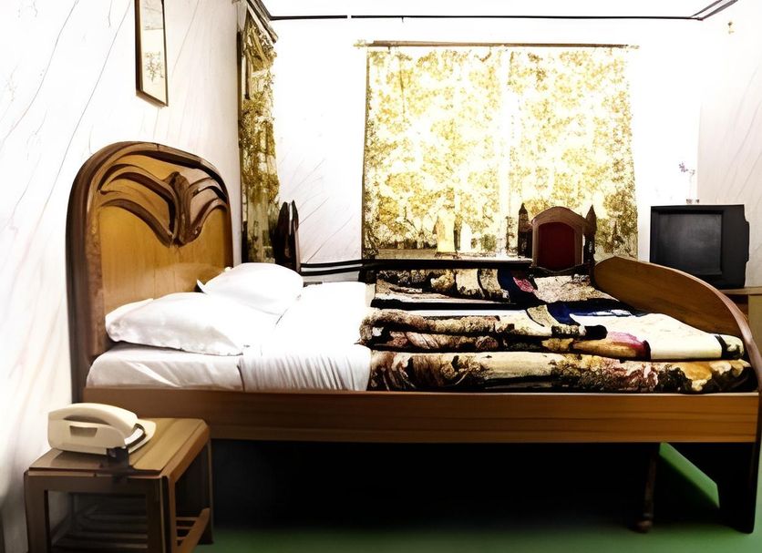 Himgiri Resorts in Dharamshala guest room with carved wooden bed, floral curtains, and TV
