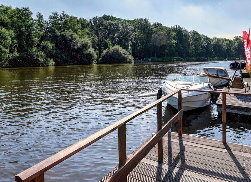 Amsterdam Lake Hotel in Badhoevedorp with docked boats on a riverside wooden deck by the water.