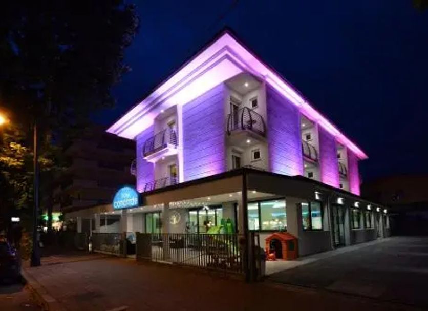 Hotel Concorde in Cesenatico, lit purple at night with a corner facade and ground-floor terrace