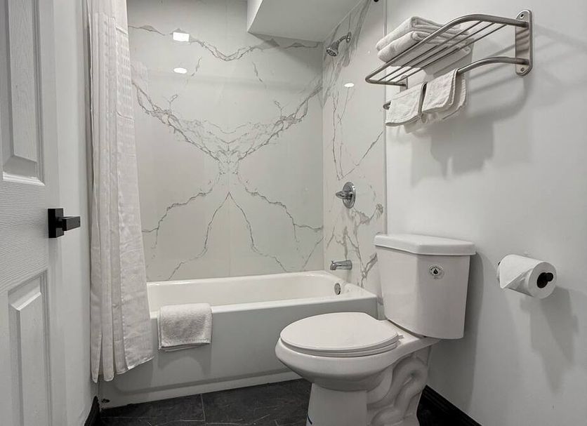 Rosemead Motel bathroom with tub-shower combo, white toilet, towel rack and wall-mounted toilet paper holder in Rosemead