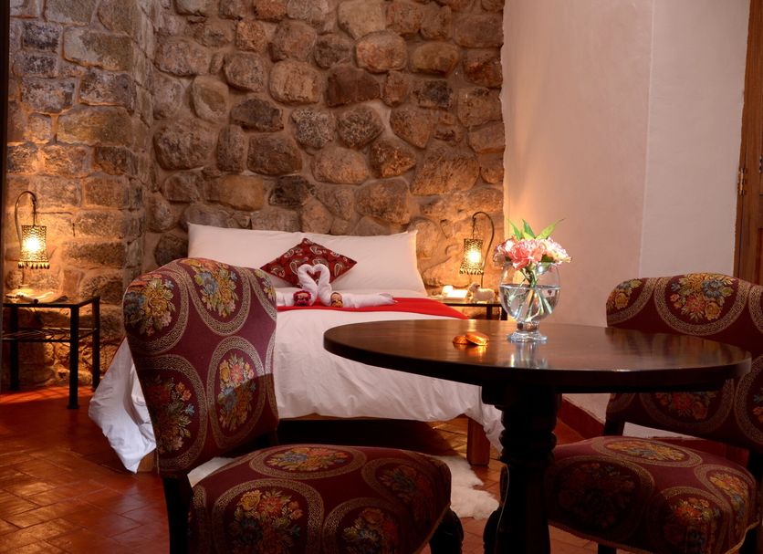 Rumi Wasi in Cusco: cozy room with stone wall, bed, round table, and patterned chairs