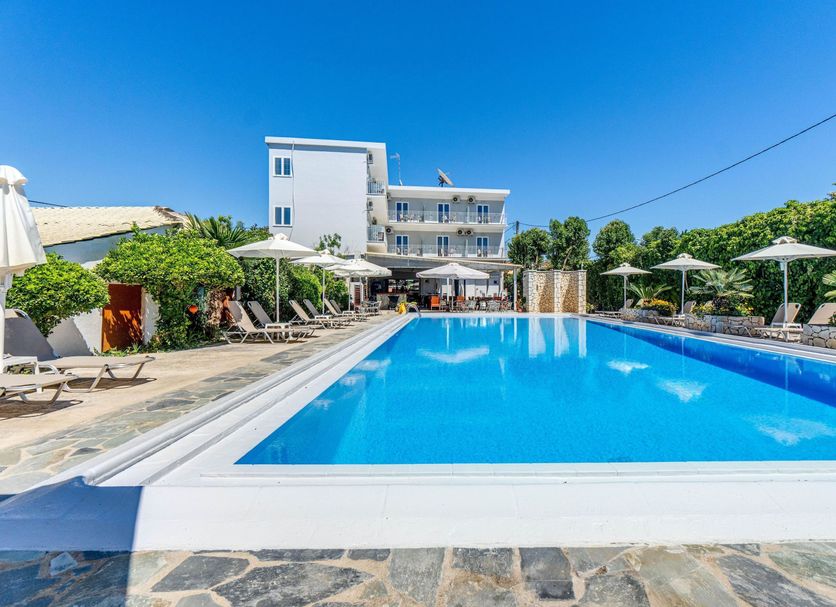 Angela Hotel & Apartments in Gouvia with a large outdoor pool, loungers, and umbrellas under a clear blue sky