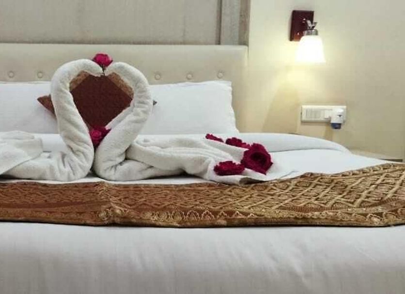 The Rass, Kanpur: bed with swan towel art, rose petals, and wall sconces in a guest room