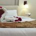 The Rass, Kanpur: bed with swan towel art, rose petals, and wall sconces in a guest room