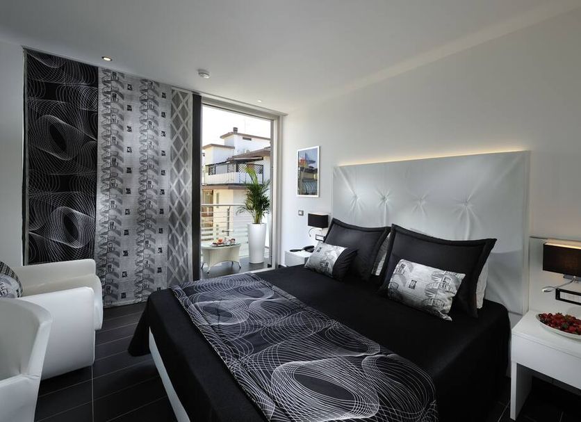 Hotel Rossini in Lignano Sabbiadoro guest room with black bed, balcony door and white armchair