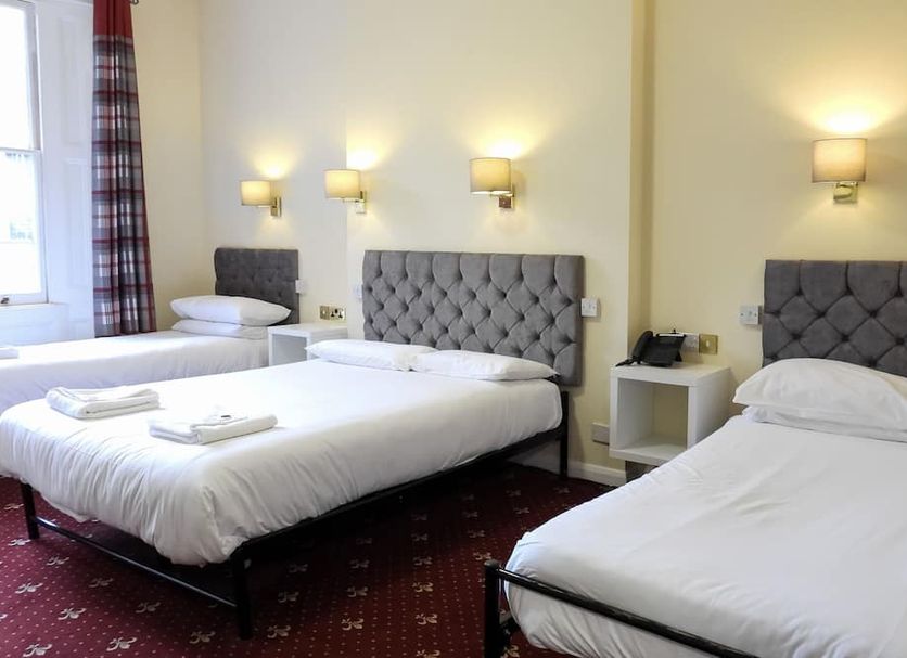 Hyde Park Court Hotel in London with three single beds in a simple guest room and wall lights