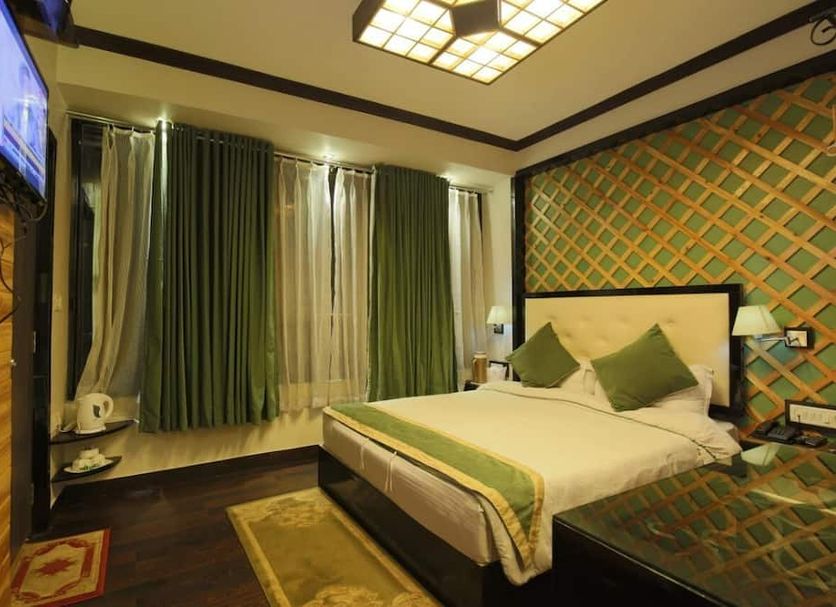 Hotel Dip Palace, Darjeeling guest room with king bed, green curtains, wall-mounted TV and patterned accent wall