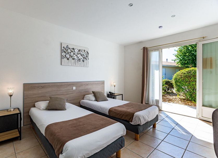 Logis Hôtel L'Oliveraie in Cognac room with twin beds and patio doors opening to a garden view.